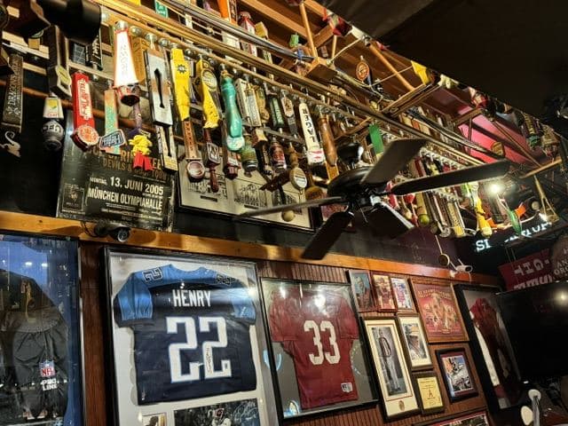 Tap handles filling the ceiling racks above a wall of framed football jerseys and photographs.