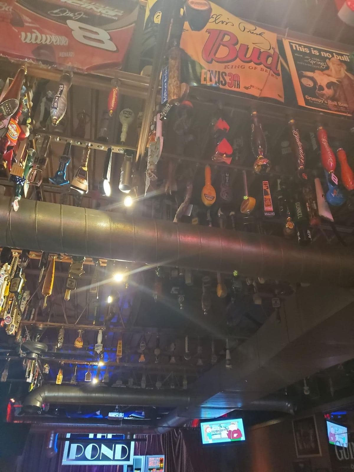 Tap handles hung in long racks across the ceiling between the ductwork, brewery banners pinned above them.