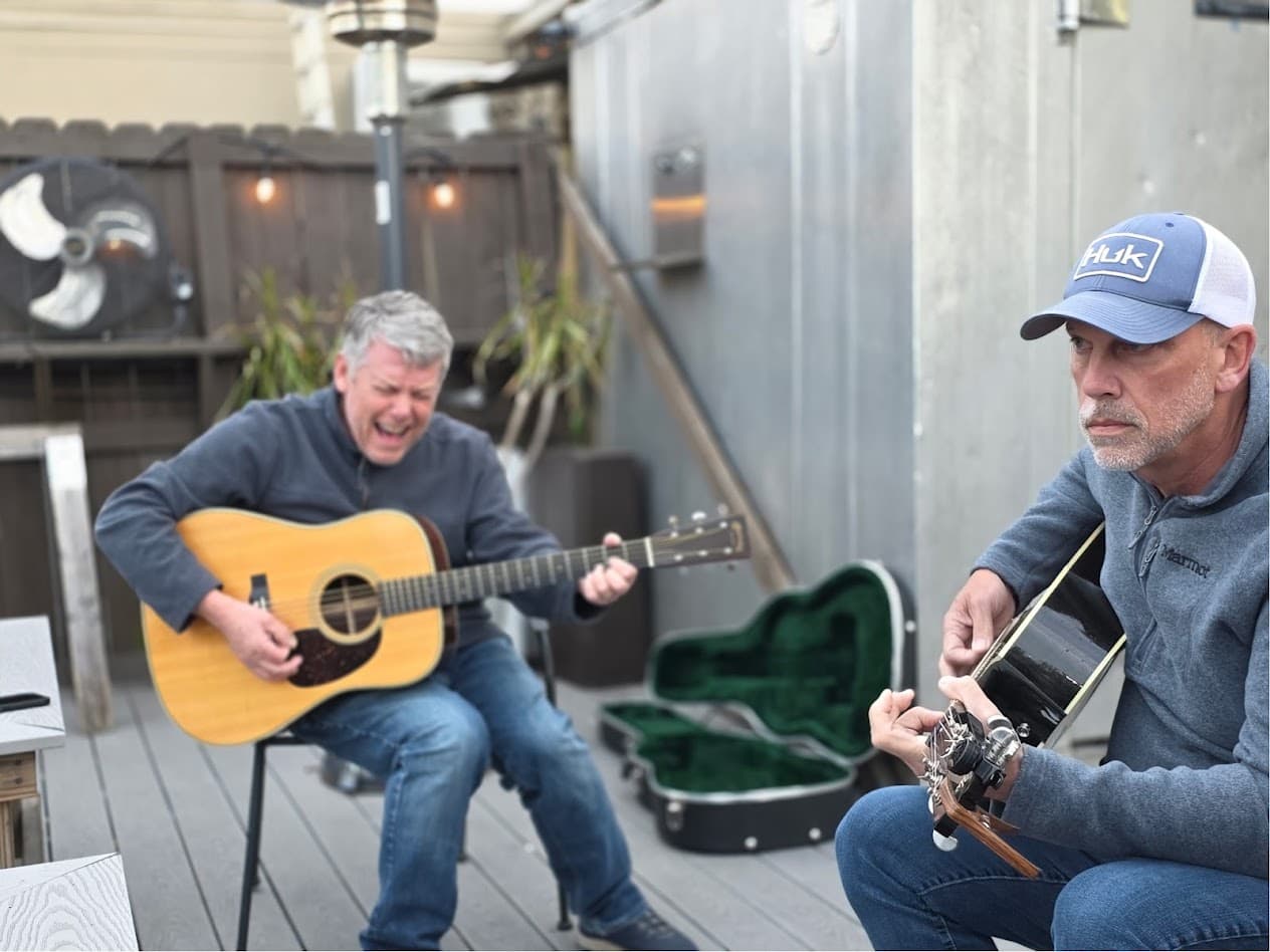 Two guitarists playing on The Pond’s outdoor patio, string lights and a patio heater on the fence behind them.