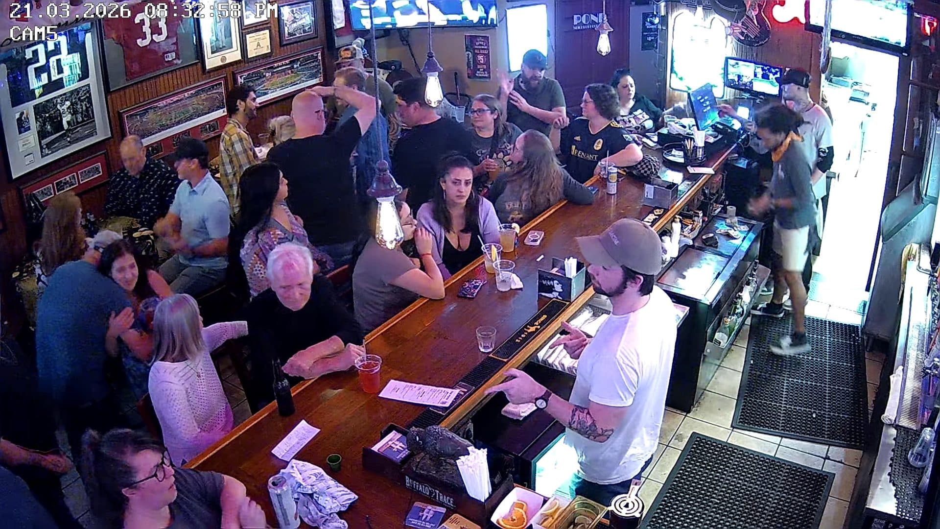 Security-camera footage of a crowded bar on a busy night, guests gathered several deep along the rail.
