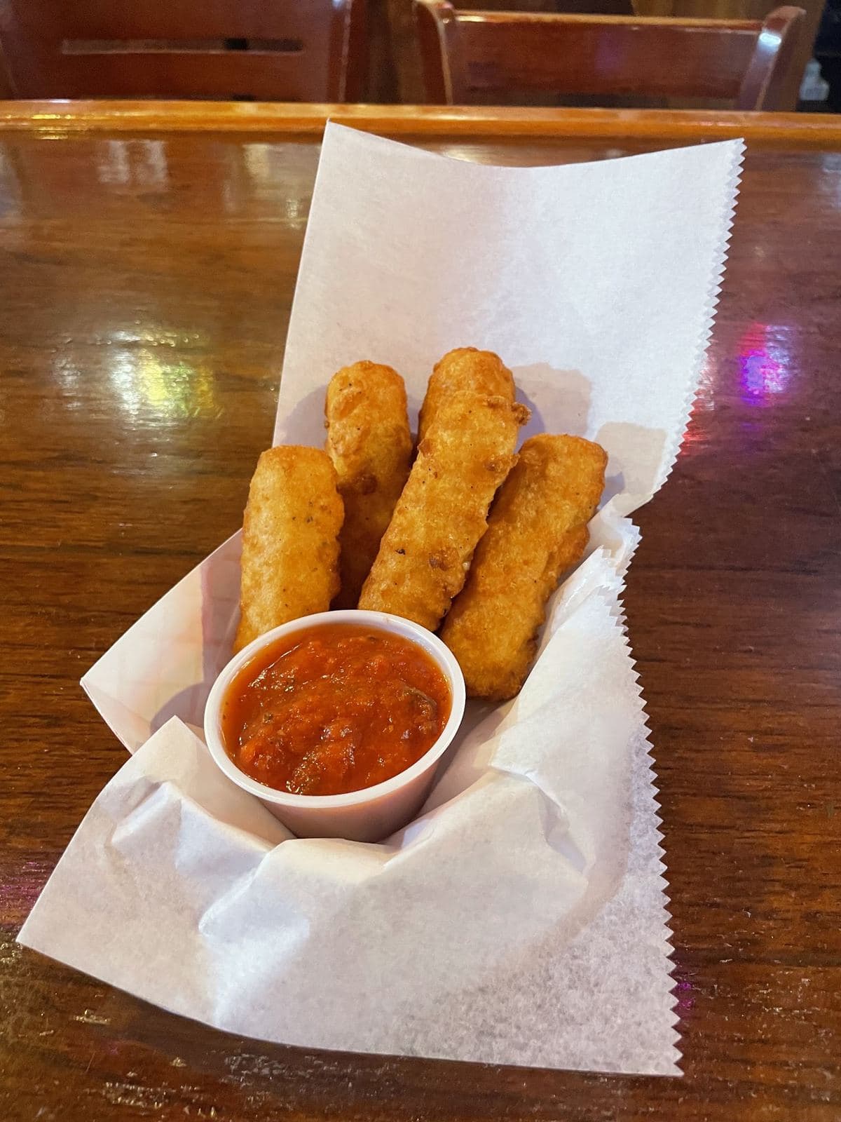 Fried mozzarella cheese sticks in a paper-lined basket with a cup of marinara.